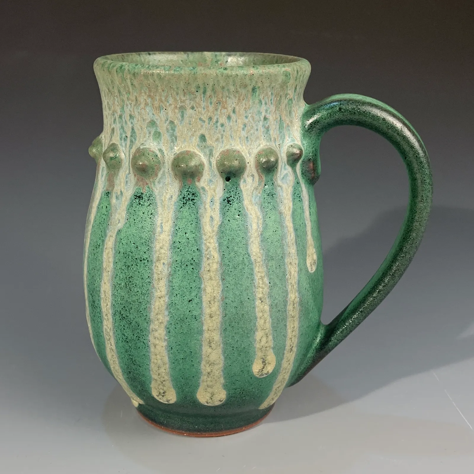 Juniper mug in deep green glaze with creamy white drips, beaded detail below the rim and a green handle.