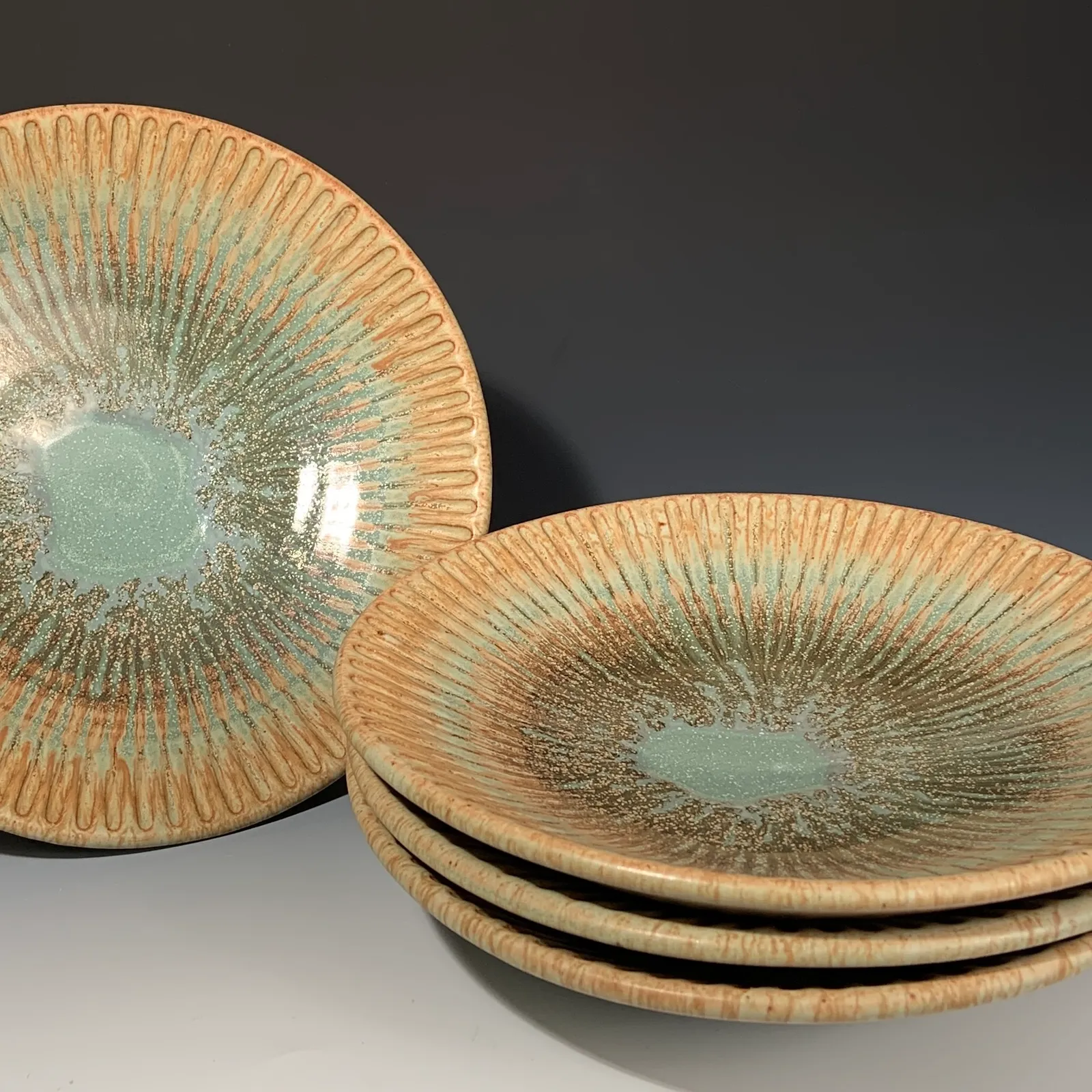 Stack of four Willow plates in jade green and ochre, with carved lines radiating from the center.